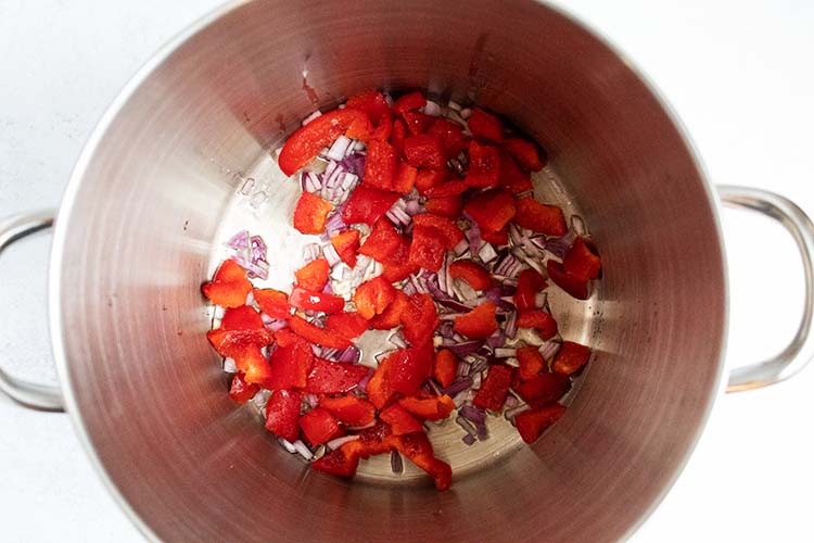 overhead view of chopped red peppers and red onions in pot 