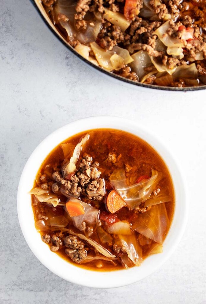 overhead view of bowl of cabbage soup with ground beef and pot of soup next to it
