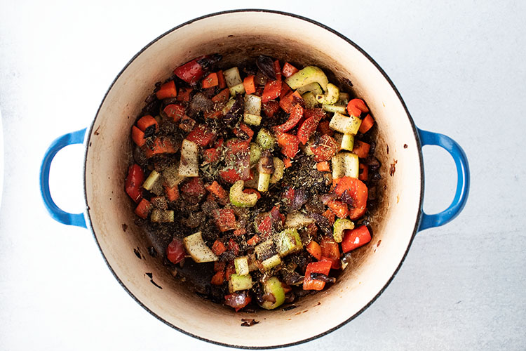 overhead view of sauteed carrots, celery, onions, and red peppers with seasoning on top in blue pot for how to make easy vegetable soup