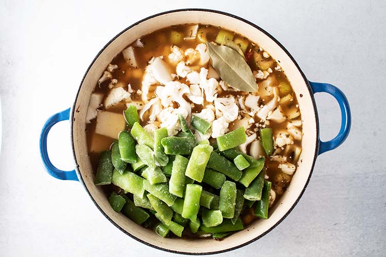 overhead view of green beans and cauliflower added to blue pot for how to make homemade vegetable soup