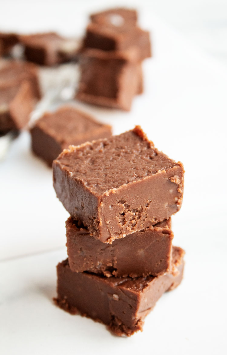 sideview of stack of three chocolate colored microwave fudge pieces on countertop with more in the background