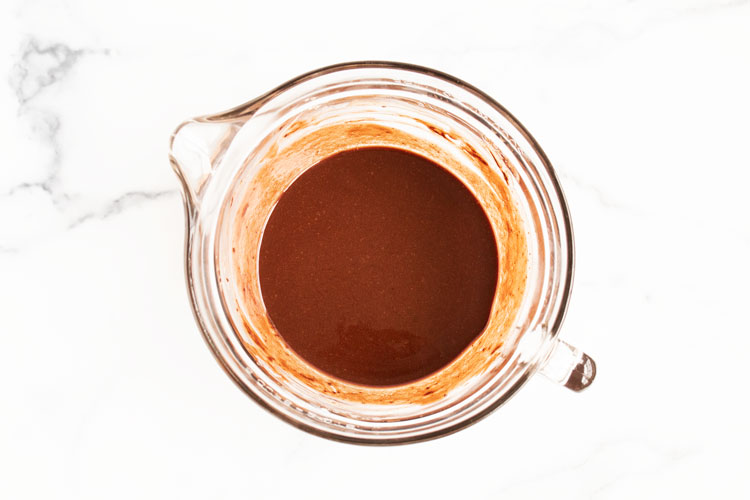 overhead view of glass measuring cup with melted chocolate inside on white countertop