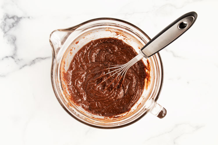 overhead view of measuring cup with melted chocolate and mixing utensil on white countertop