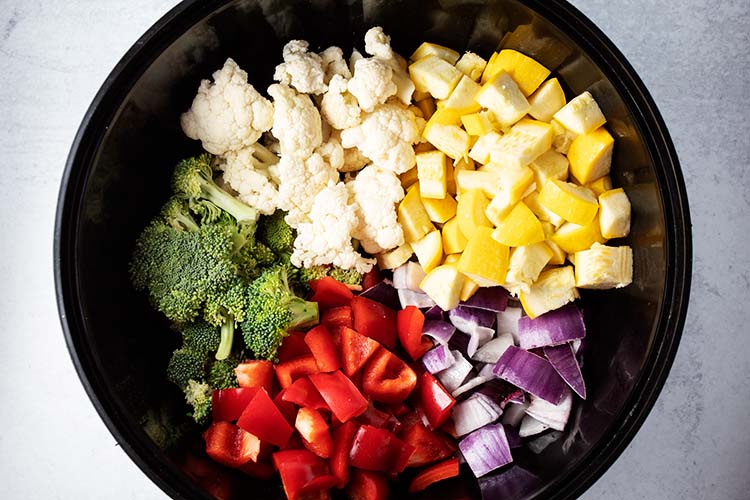 overhead view of ingredients needed for oven roasted vegetables recipe including broccoli, cauliflower, summer squash, red peppers and red onions
