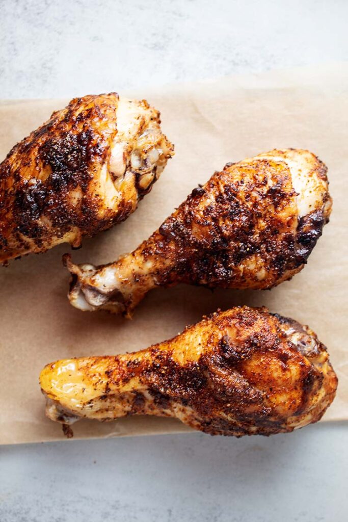 overhead view of 3 crispy pieces of air fryer chicken legs on tan parchment paper laying on white countertop