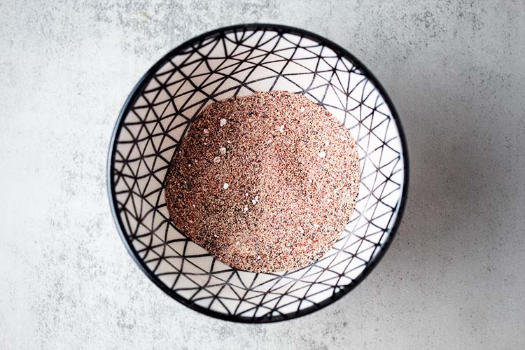 overhead view of chicken powder seasoning mix in a white bowl with black lines as decore on a white marble countertop