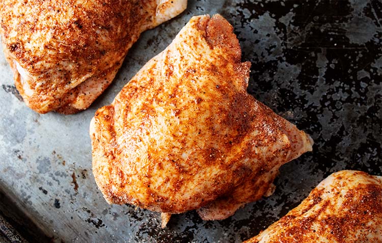 overhead view of brown seasoning mix on three chicken thighs laying on a sheet pan