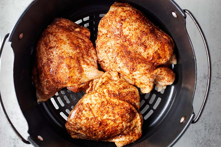 overhead view of  three partially cooked brown chicken thighs in a black air fryer basket