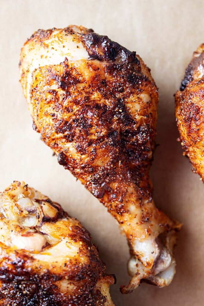 overhead view of 3 crispy pieces of air fryer chicken legs on tan parchment paper