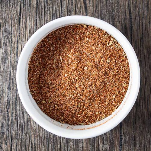overhead view of chili powder seasoning mix inside of white bowl on wooden table