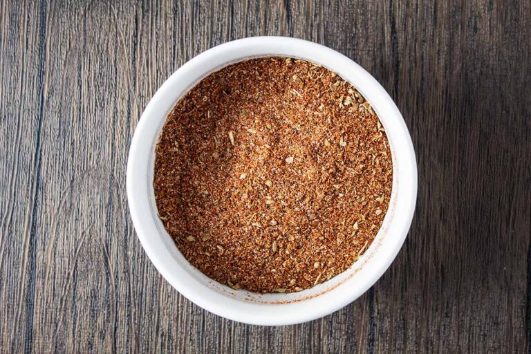 overhead view of chili powder seasoning mix inside of white bowl on wooden table