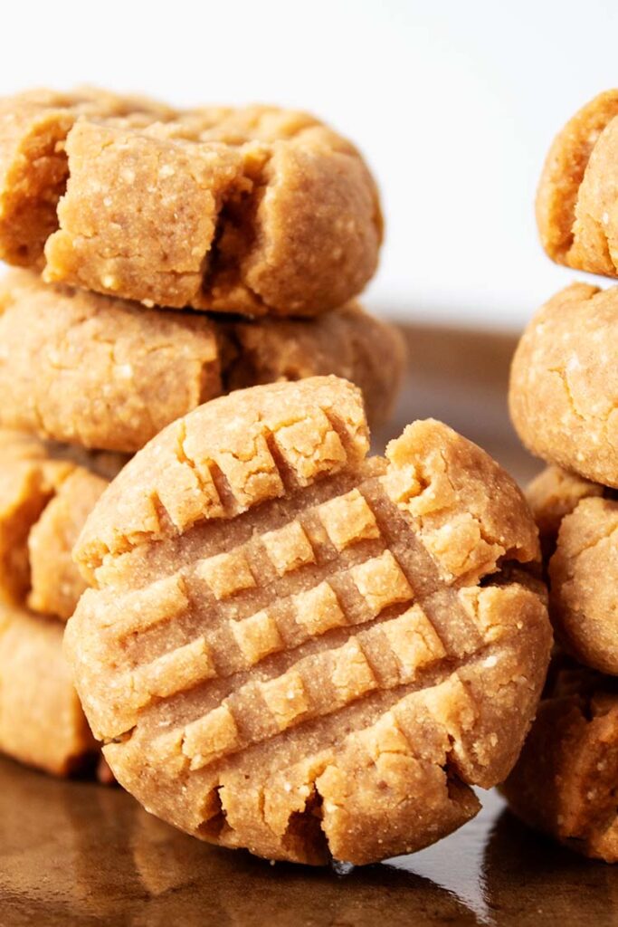 sideview of two stacks of four tan peanut butter cookies and one cookie in foregroud with fork mark pattern standing upright, all on brown sheetpan