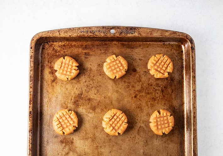 overhead view of brown sheet pan with six flattened brown peanut butter cookies spaced out
