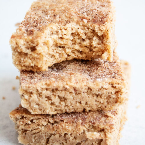 sideview of three tan colored snickerdoodle bars with a bit taken out of the top one on a white countertop