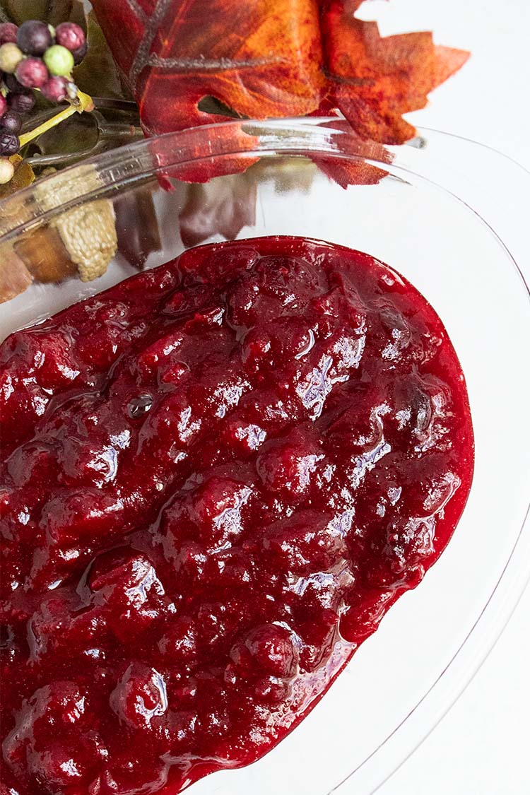 overhead view of homemade cooked cranberry sauce in clear serving dish with fall leaves decor next to it on a white countertop