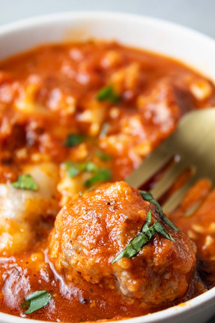 side view meatball casserole in white bowl and gold serving spoon