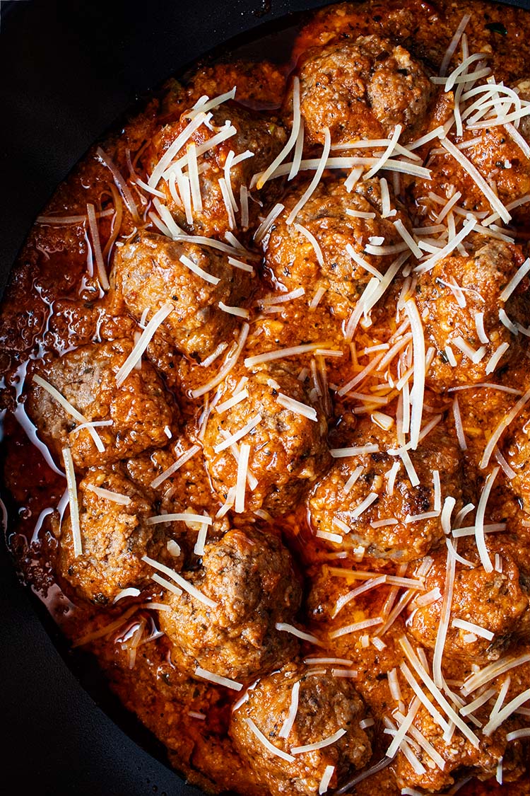 overhead view of homemade meatballs in skillet mixed with marinara sauce and topped with shredded parmesan