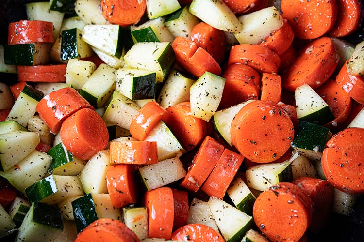 overhead view of zucchini and carrots with seasoning ready for roasting