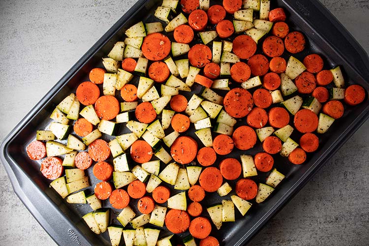 overhead view of carrots and zucchini on baking sheet ready to be roasted
