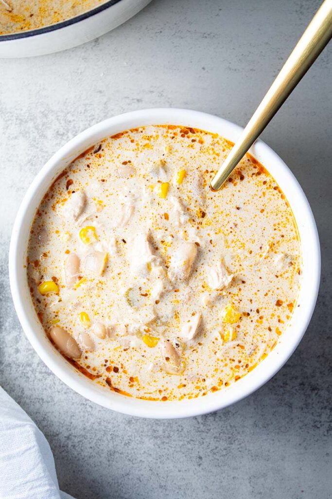 overhead view of serving bowl of white chicken chili with gold spoon inside