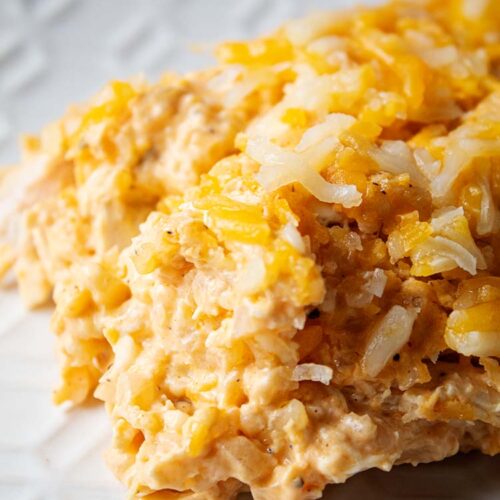 sideview of a serving of buffalo chicken casserole with cauliflower on a white serving dish