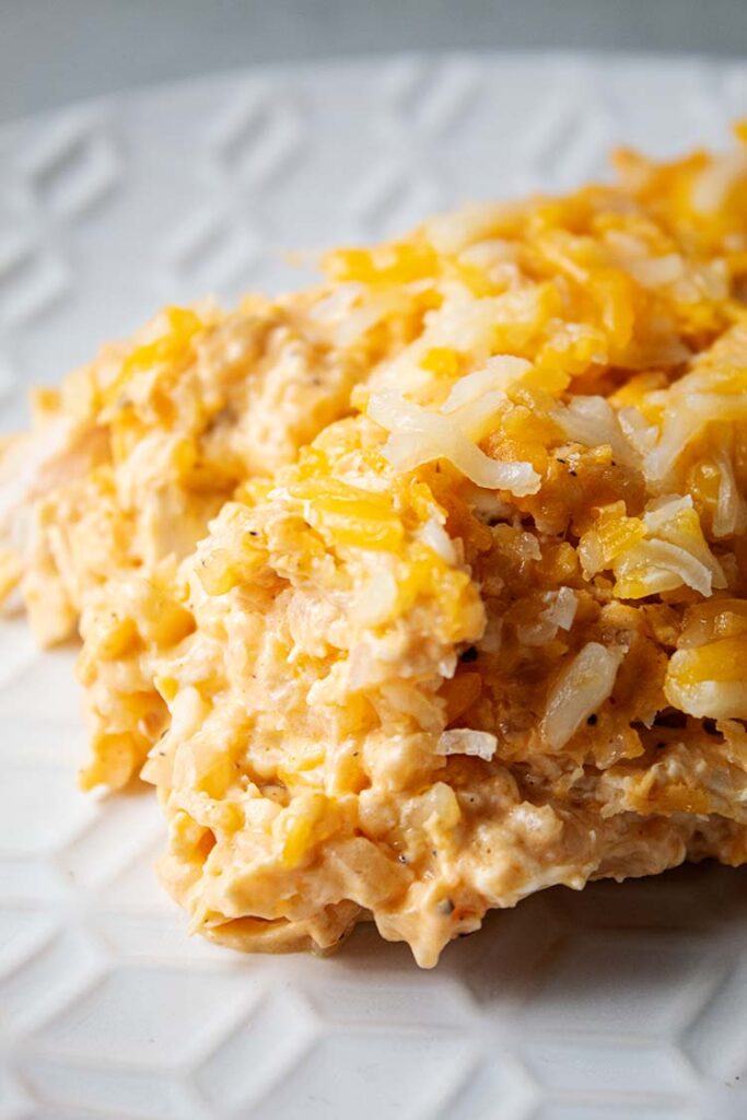 sideview of a serving of buffalo chicken casserole with cauliflower on a white serving dish
