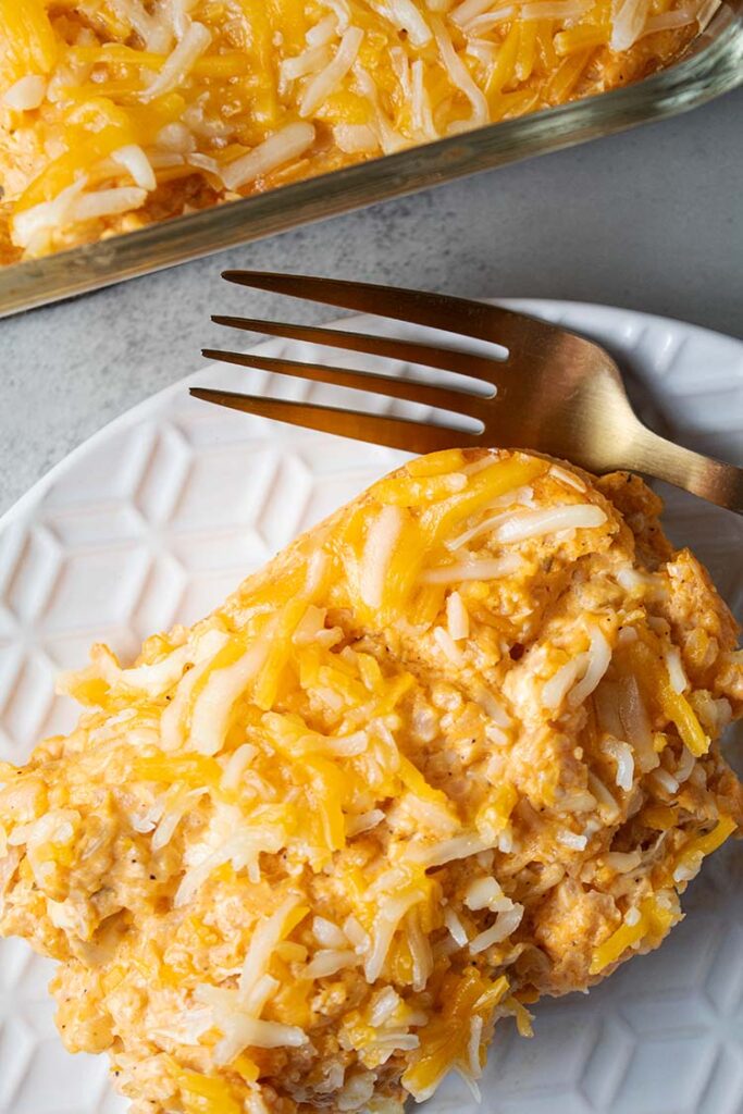 overhead view of a serving of buffalo chicken casserole with cauliflower rice on a white serving dish and gold fork laying on the side