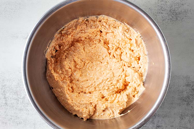 overhead view of steel mixing bowl with combined ingredients including cream cheese, sour cream, spices and buffalo sauce for buffalo chicken casserole recipe