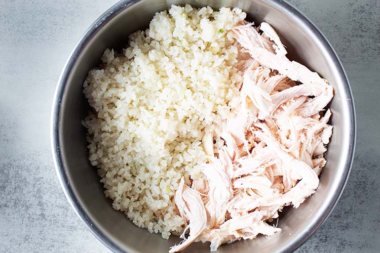 overhead view of metal mixing bowl with shredded chicken and cauliflower rice added to previously whipped ingredients for buffalo chicken casserole recipe