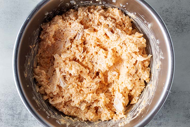 overhead view of metal mixing bowl with shredded chicken and cauliflower rice added to previously whipped ingredients for buffalo chicken casserole recipe