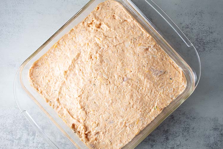 overhead view of metal mixing bowl with shredded chicken and cauliflower rice mixed with other ingredients for buffalo chicken casserole recipe
