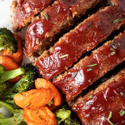 overhead view of turkey meatloaf on a white serving dish with ketchup glaze and healthy carrots and broccoli on the side