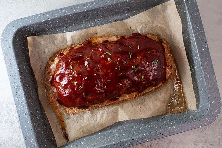 overhead view of fully baked turkey meatloaf on parchment paper in a baking pan with ketchup glaze spread on top