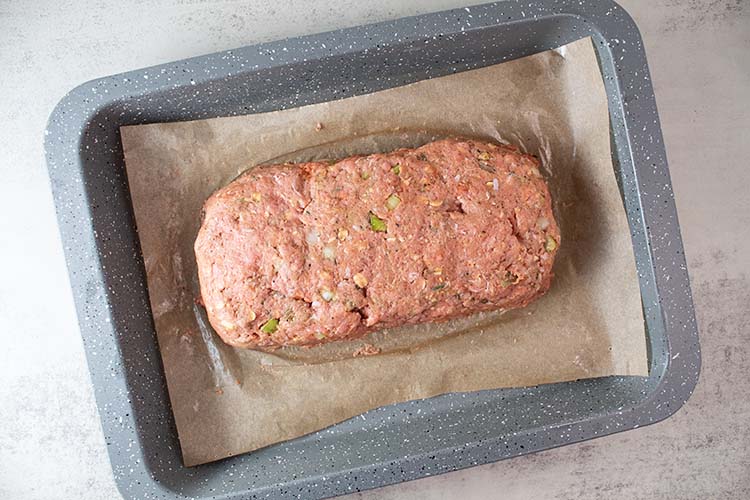 overhead view of ground turkey mixture formed into a turkey loaf on parchment paper in a baking pan