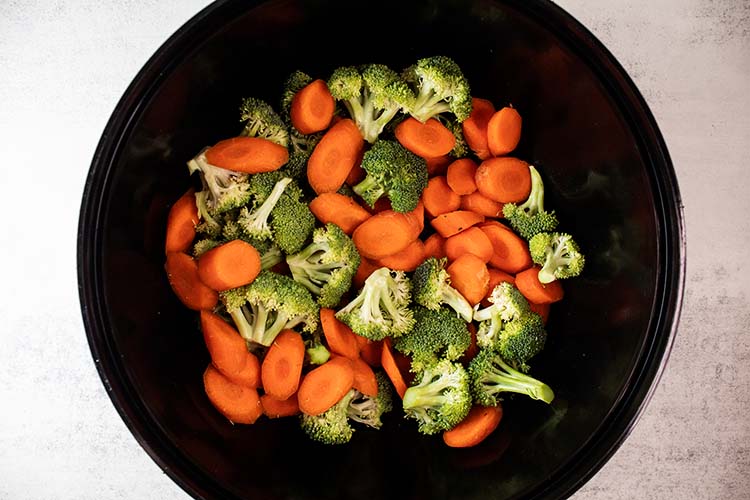 overhead view of chopped broccoli and carrots in black mixing bowl