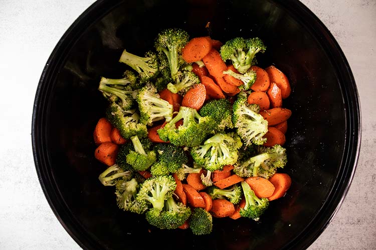 overhead view of broccoli and carrots in black mixing bowl and mixed with seasoning