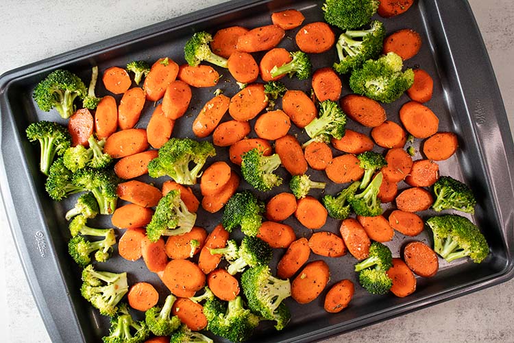 overhead view of seasoned broccoli and carrots on metal sheet pan ready to be roasted