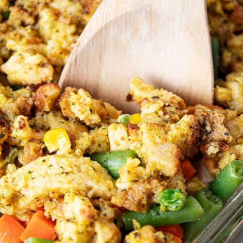 sideview of chicken and stuffing casserole in glass casserole dish with wooden serving spoon removing a piece