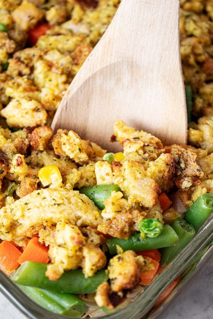 sideview of chicken and stuffing casserole in glass casserole dish with wooden serving spoon removing a piece