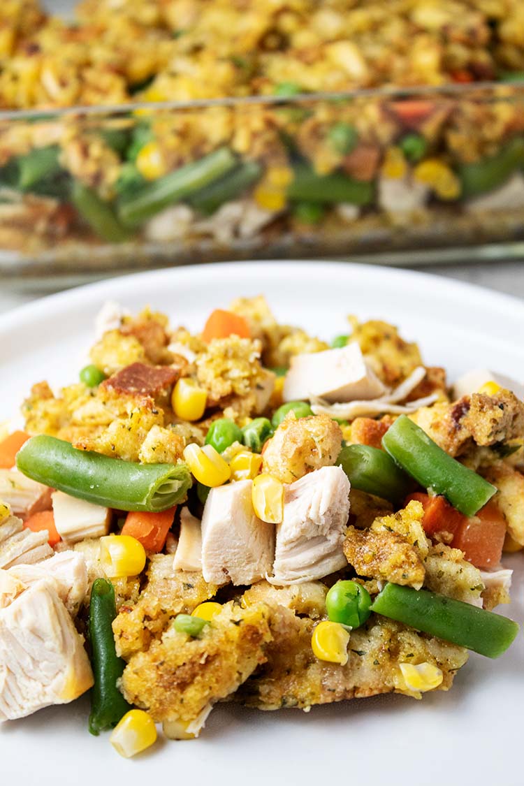 sideview of serving of chicken stuffing casserole on white dish with remaining casserole in background