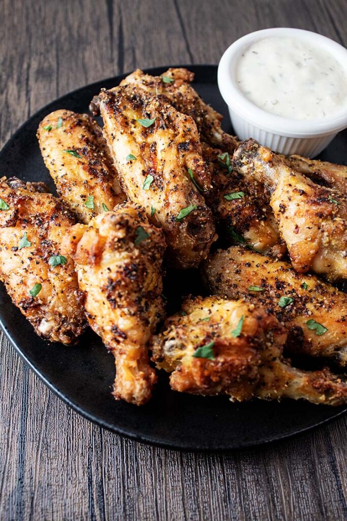 sideview of a black serving plate with air fryer lemon pepper wings and a side of blue cheese in a small white condiment cup