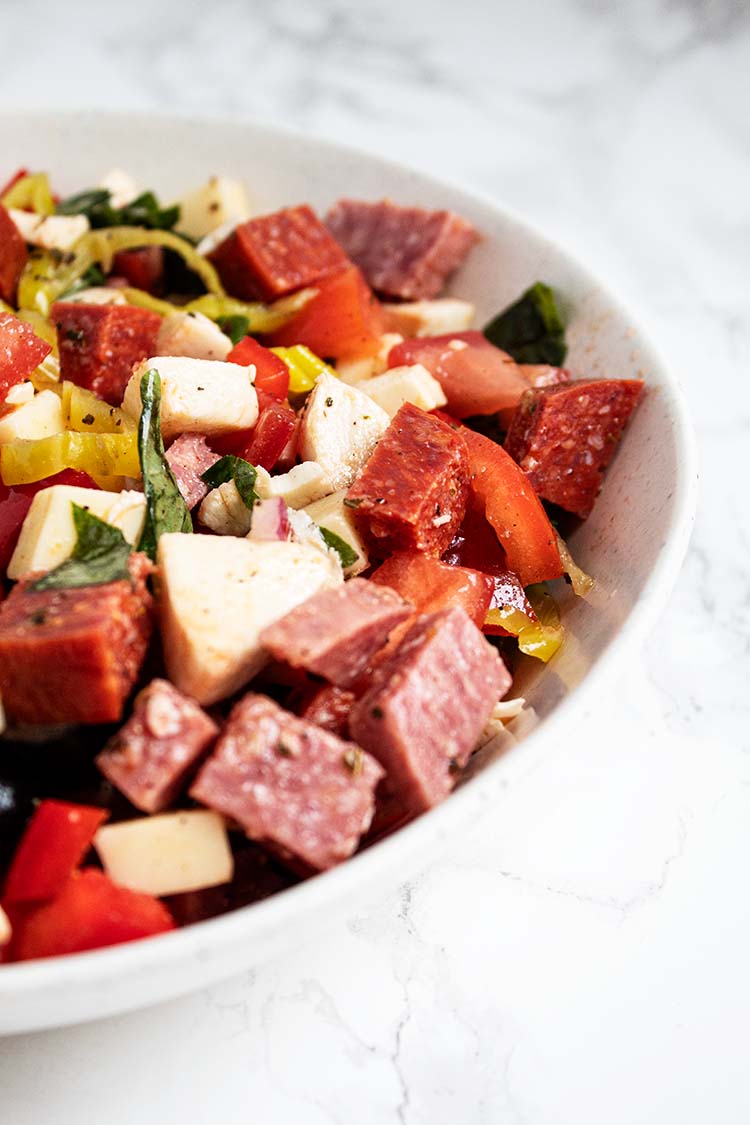 sideview of authentic classic italian antipasto salad in white serving bowl on a white countertop