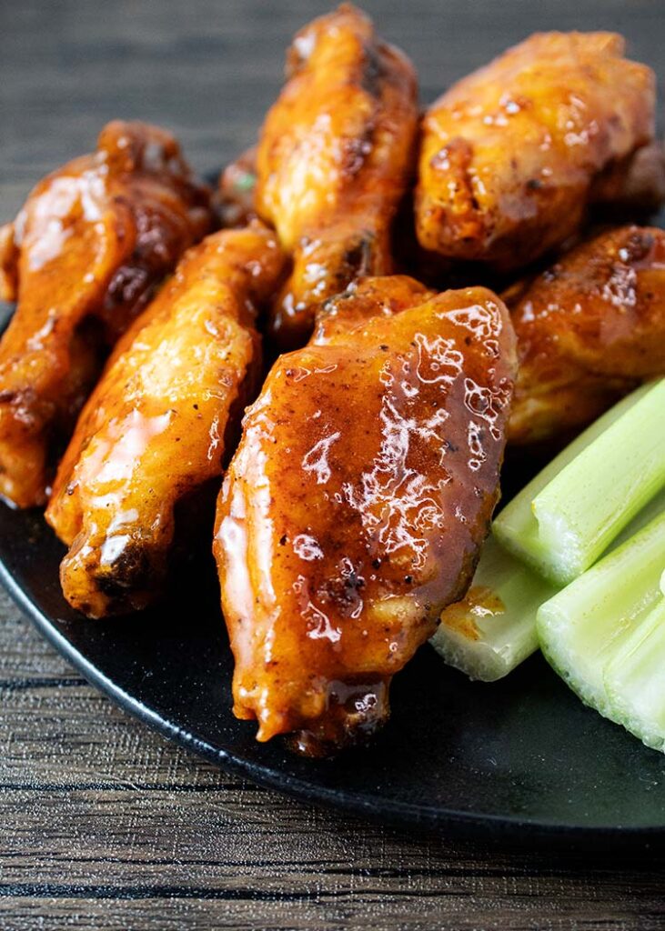 sideview of air fryer buffalo wings served on a black plate with celery on the side