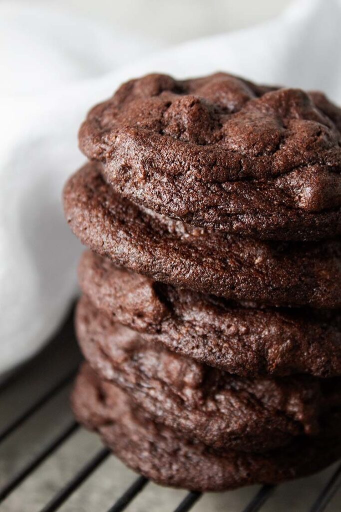 sideview of stack of five chocolate chocolate chip cookies on a wire cooling rack with white cloth napkin in background