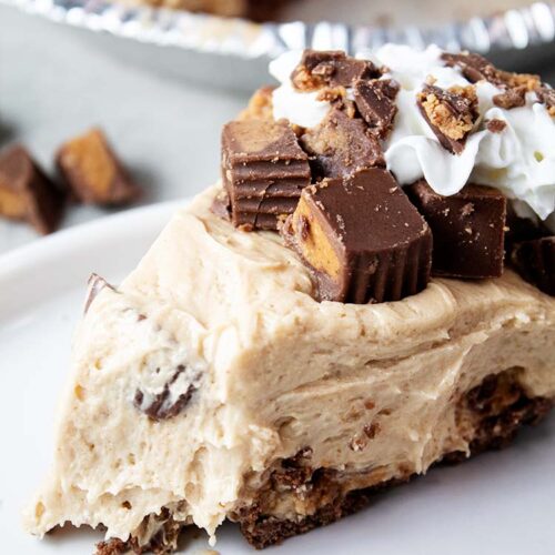 sideview of no bake peanut butter pie using cool whip topped with chopped reese's cups and whipped cream and one bite taken out