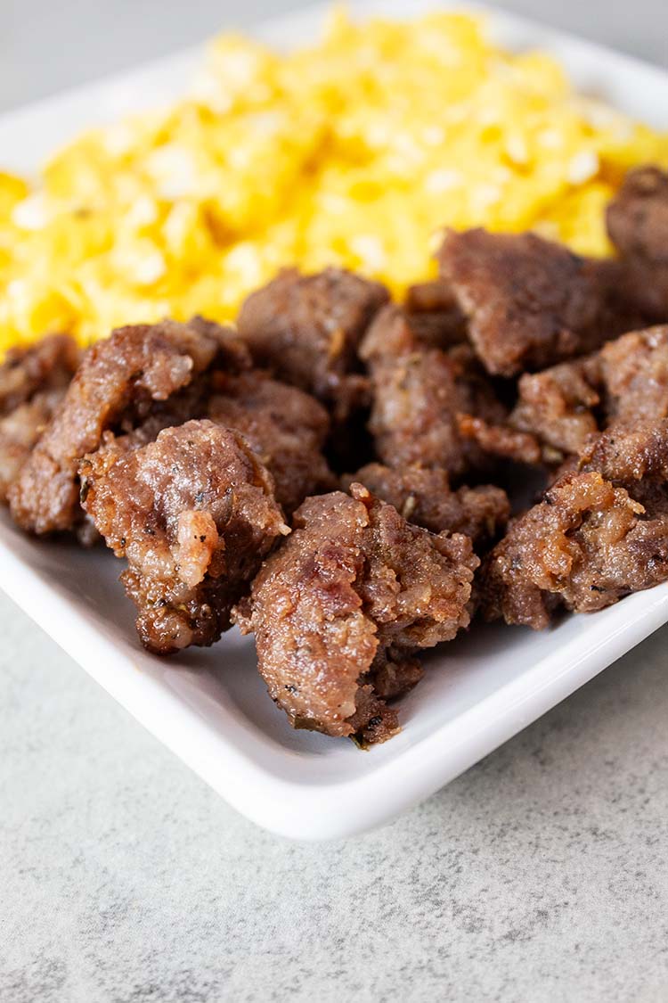 sideview of italian sausage on a square white serving dish with scrambled eggs on the side
