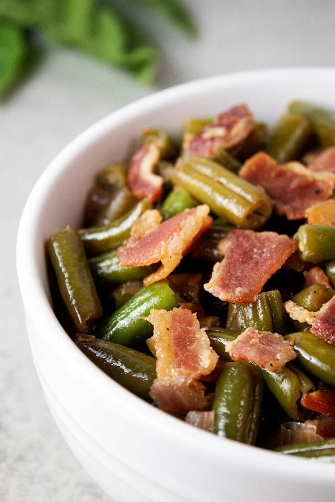 sideview of bacon green beans in a white serving bowl