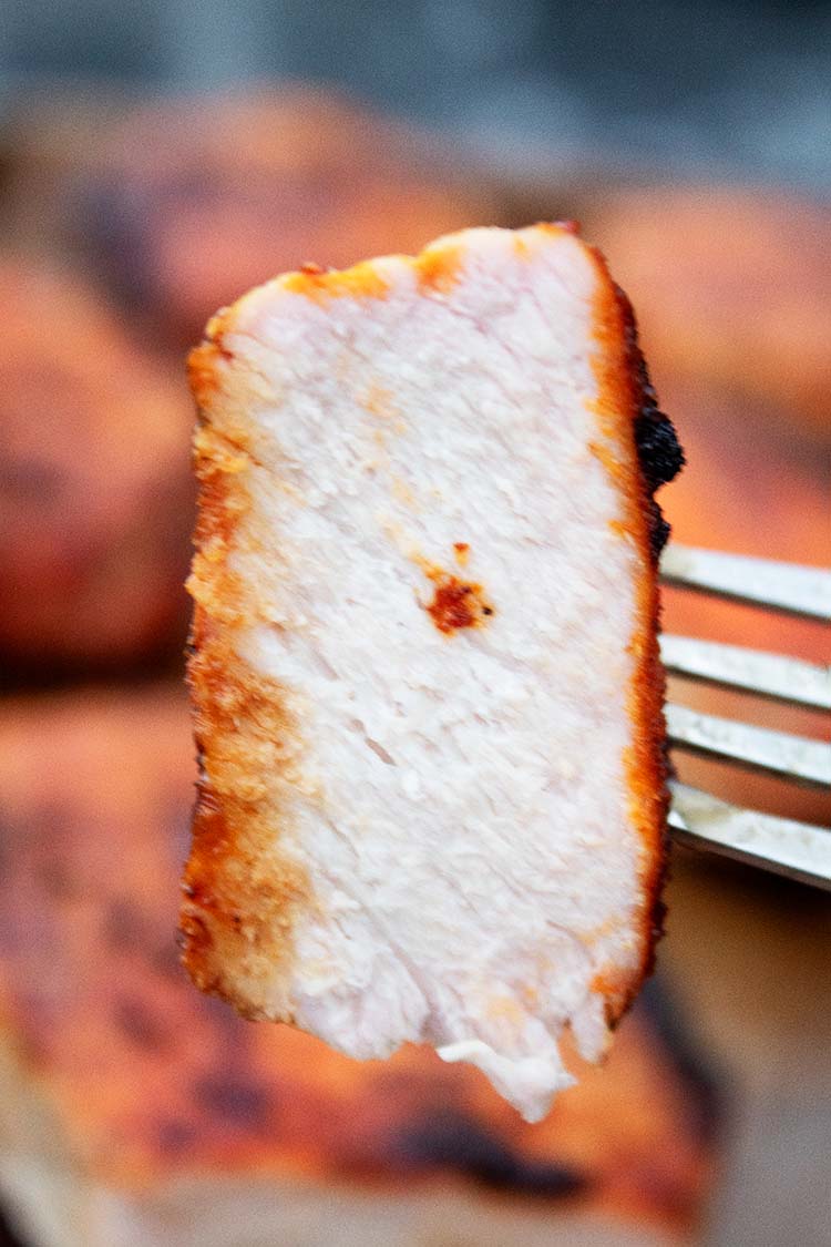 sideview of sliced off piece of grilled pork chops held up with a fork to show the juicy white meat center