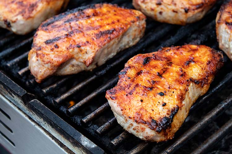 sideview of grilled pork chops lined up on the grill in two rows