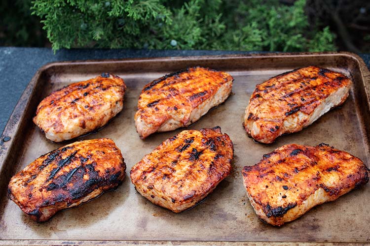 sideview of six grilled pork chops cooling on a sheet pan